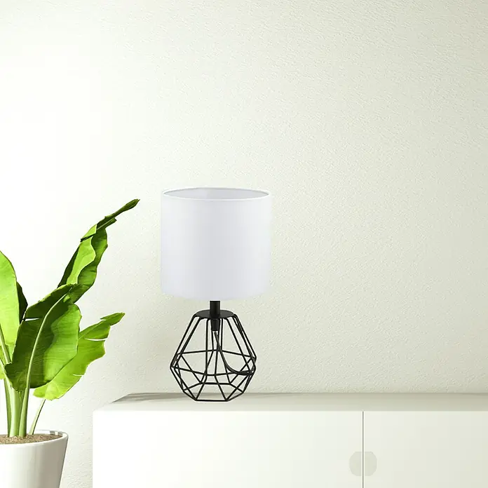 Eglo Lámpara de sobremesa Carlton 2 - 60 W, L x An x Al: 16,5 x 16,5 x 30,5 cm, Negro, E14 - Primer plano de una lámpara de mesa moderna con base metálica geométrica y pantalla blanca, colocada sobre una cómoda blanca junto a una planta de interior.