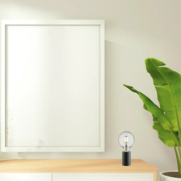 Nordlux Lámpara de sobremesa Siv Mármol - 60 W, L x An x Al: 6 x 6 x 10,3 cm, Negro, E27 - Un ambiente moderno con una elegante lámpara de bombilla sobre un aparador, complementado con un marco de fotos y una planta de interior.