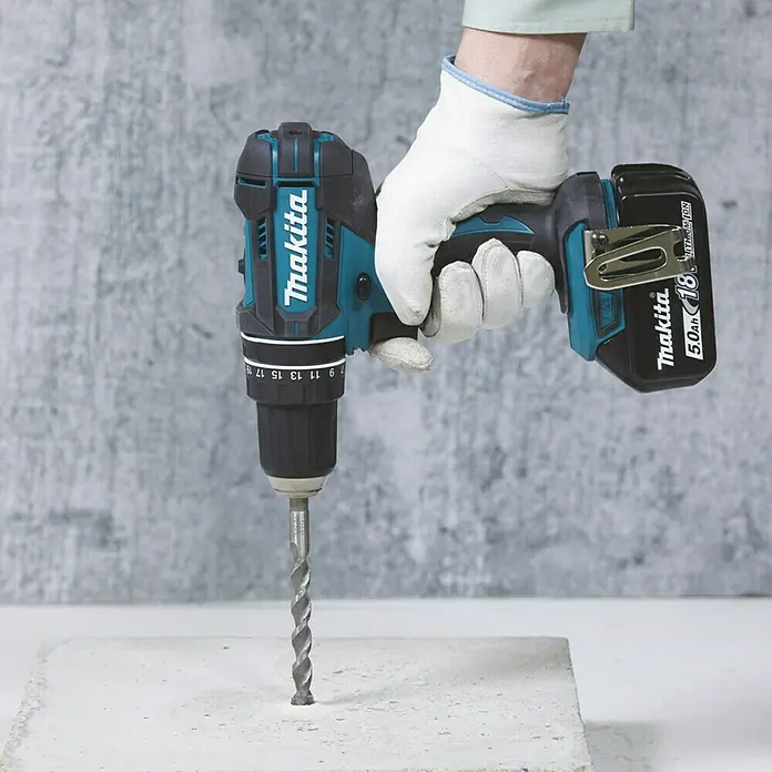 Makita LXT 18V Akku-Schlagbohrschrauber DHP482RFX9 - 18 V, 2 Akkus, 3 Ah - Makita Akku-Bohrschrauber im Einsatz beim Bohren in Beton, gehalten von einer Hand mit Arbeitshandschuh. Kraftvolles Werkzeug für Heimwerker und Profis.