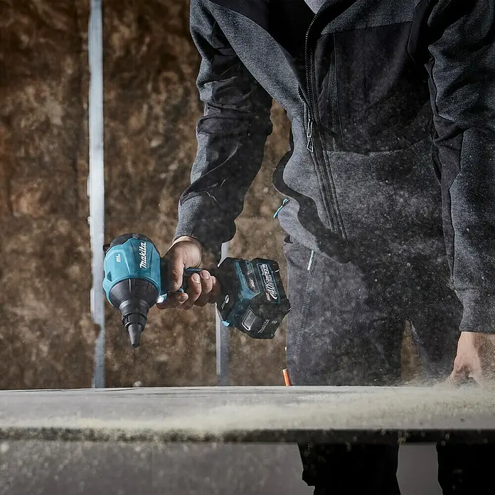 Makita XGT 40V max. Akku-Gebläse AS001GZ - 40 V, Ohne Akku - Nahaufnahme eines Makita-Akku-Trockenbauschraubers in Aktion, Staub wirbelt auf. Ideal für den professionellen Innenausbau.