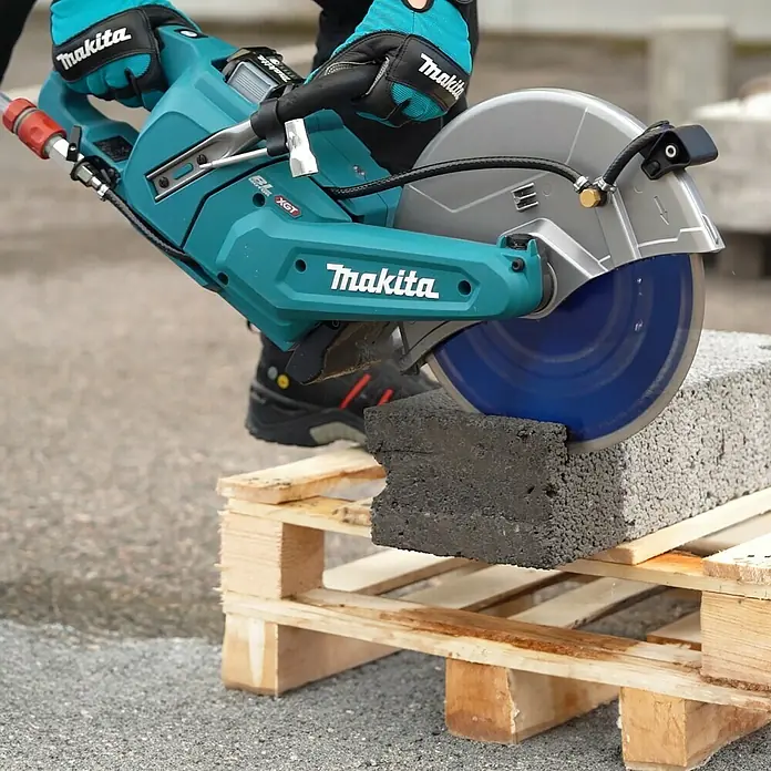 Makita XGT 40V max. Akku-Trennschleifer CE004GZ - Ohne Akku - Auf dem Bild ist eine Makita-Trennsäge zu sehen, die einen Stein schneidet. Die Säge ist blaugrün und hat ein silbernes Schutzgehäuse.