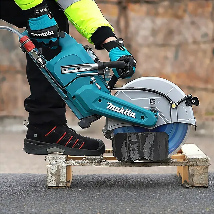 Makita XGT 40V max. Akku-Trennschleifer CE004GZ - Ohne Akku - Eine Makita Betonsäge im Einsatz, die durch einen dunklen Ziegelstein schneidet. Der Bediener trägt Schutzkleidung.