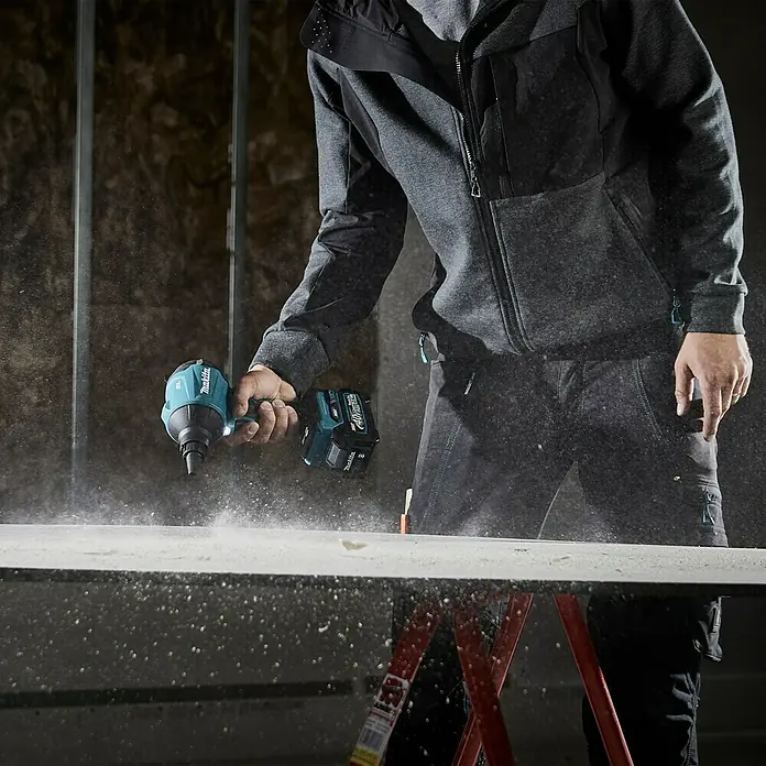 Makita XGT 40V max. Akku-Gebläse AS001GZ - 40 V, Ohne Akku - Ein Handwerker benutzt einen Makita Akku-Schlagschrauber, um an einem Projekt zu arbeiten. Staubpartikel fliegen in der Luft.