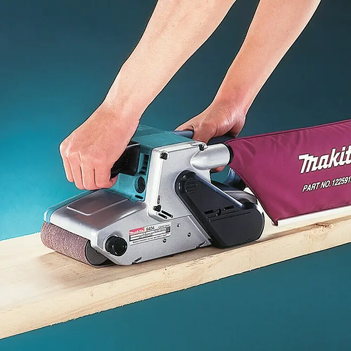 Makita Elektro-Bandschleifmaschine 9404J - 1.010 W - Eine Makita Bandschleifmaschine wird von einer Person auf einem Holzbrett bedient.