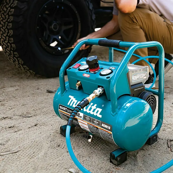 Makita XGT 40V max. Compresor de batería AC001GZ - 40 V, Sin batería, 9,3 bar - Un primer plano de un compresor de aire inalámbrico Makita AC001G, de pie sobre un suelo arenoso mientras infla un neumático.