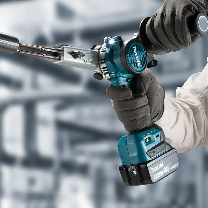 Makita LXT 18V Akku-Bandfeile DBS180Z - 18 V, Ohne Akku, Bandgeschwindigkeit: 600 m/min - 1.700 m/min - Nahaufnahme einer Makita Rohrbiegemaschine mit Akku, die von einer Person mit Arbeitshandschuhen bedient wird.