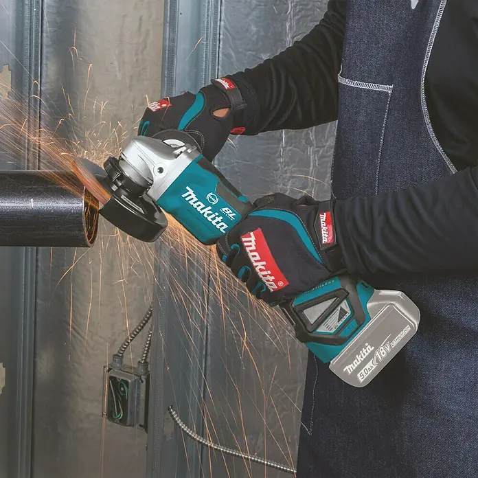 Makita LXT 18V Akku-Winkelschleifer DGA517Z - Ohne Akku, Durchmesser Scheibe: 125 mm - Ein Mann benutzt einen Makita Akku-Winkelschleifer, um ein Metallrohr zu bearbeiten, wobei Funken fliegen. Er trägt eine Schürze und Schutzhandschuhe.