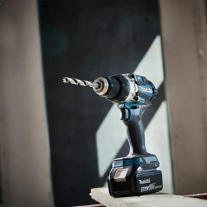 Makita LXT 18V Akku-Schlagbohrschrauber DHP489RTJ - 18 V, 2 Akkus, 5 Ah, 73 Nm - Nahaufnahme eines Makita Akku-Bohrschraubers mit eingesetztem Bohrer, der auf einem Holzbrett steht.