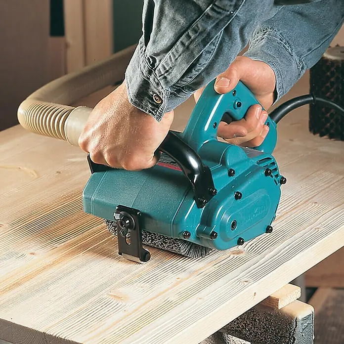 Makita Renovierungsschleifer 9741J - Leerlaufdrehzahl: 3.500 U/min, 860 W - Detailaufnahme einer Makita Bürstenschleifmaschine beim Bearbeiten einer Holzoberfläche mit Absaugvorrichtung.