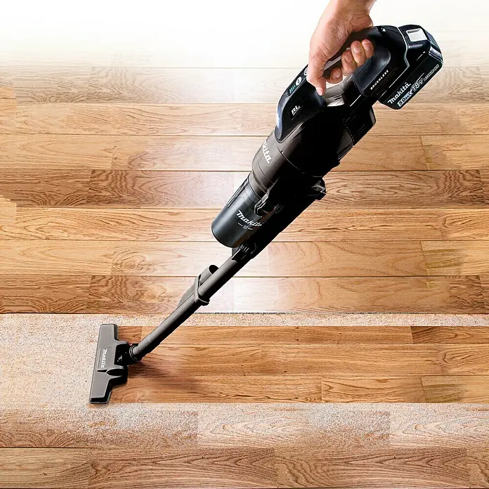 Makita LXT 18V Akku-Staubsauger mit Zykloneinheit DCL286FZW - 18 V, Ohne Akku, Behältervolumen: 0,25 l - Akkusauger von Makita in Schwarz wird auf einem Holzboden mit verstreutem Staub verwendet, um ihn zu reinigen.