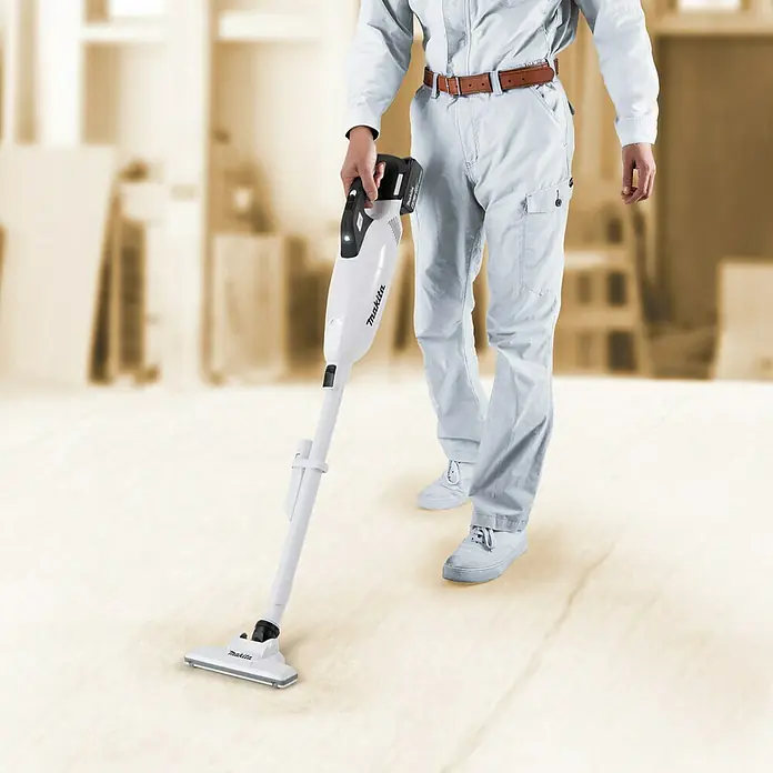 Makita LXT 18V Akku-Staubsauger DCL283FZ - 18 V, Ohne Akku, Behältervolumen: 0,75 l - Ein Mann in Arbeitskleidung benutzt einen Makita Akku-Staubsauger auf einem hellen Holzboden, um Staub und Schmutz zu beseitigen.