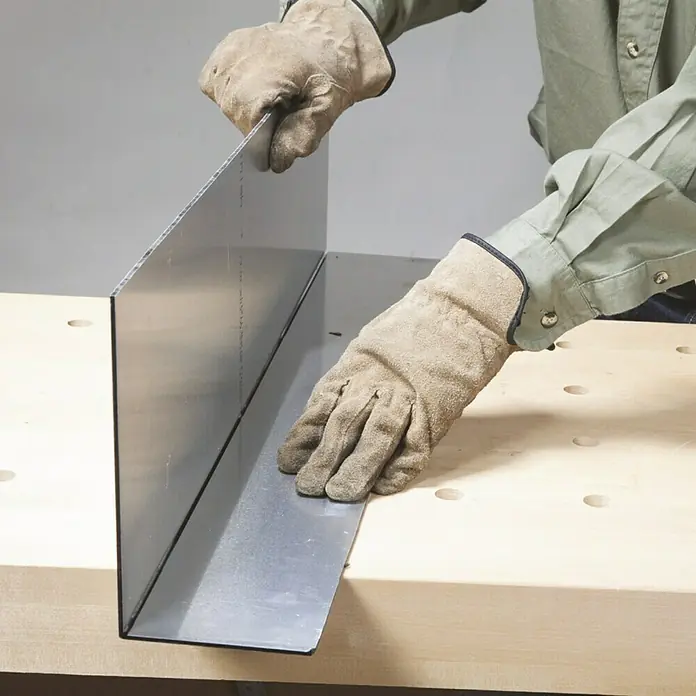 Makita Plattenfräse CA5000XJ - 1.300 W, Leerlaufdrehzahl: 2.200 U/min - 6.400 U/min - Eine Person mit Handschuhen, die ein Stück gefalztes Metall auf einem Tisch hält.