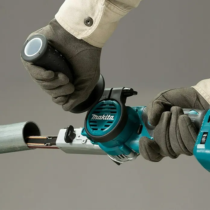 Makita LXT 18V Akku-Bandfeile DBS180Z - 18 V, Ohne Akku, Bandgeschwindigkeit: 600 m/min - 1.700 m/min - Nahaufnahme eines Makita-Bandschleifers in Aktion, der Metallrohre bearbeitet. Fachmännisches Werkzeug für präzise Schleifarbeiten.