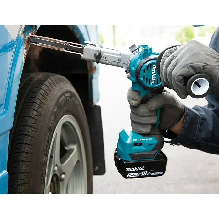 Makita LXT 18V Akku-Bandfeile DBS180Z - 18 V, Ohne Akku, Bandgeschwindigkeit: 600 m/min - 1.700 m/min - Der Makita Akku-Bandschleifer DBS180ZJ schleift Rost an einem blauen Auto. Perfekt für die Kfz-Reparatur mit 18V Akku.