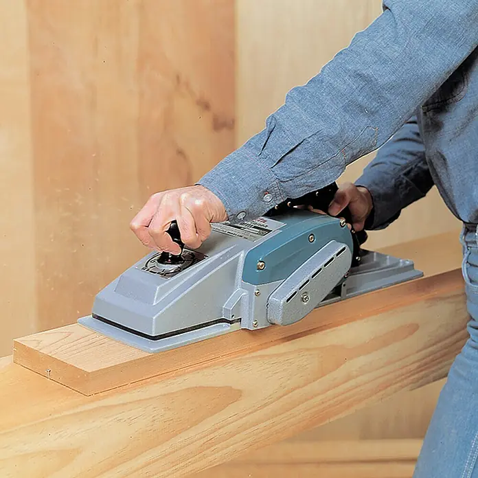 Makita Elektrohobel 1806B - 840 W, Leerlaufdrehzahl: 0 U/min - 16.000 U/min - Der Handwerker benutzt einen elektrischen Hobel, um ein Holzbrett zu bearbeiten, wodurch eine glatte Oberfläche entsteht.