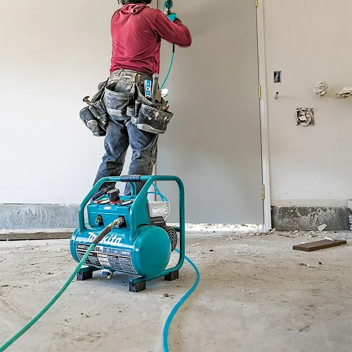 Makita XGT 40V max. Akku-Kompressor AC001GZ - 40 V, Ohne Akku, 9,3 bar - Der leise Makita-Kompressor AC001G, ein tragbares, ölfreies Gerät mit blauem Gehäuse, steht auf einer Baustelle.