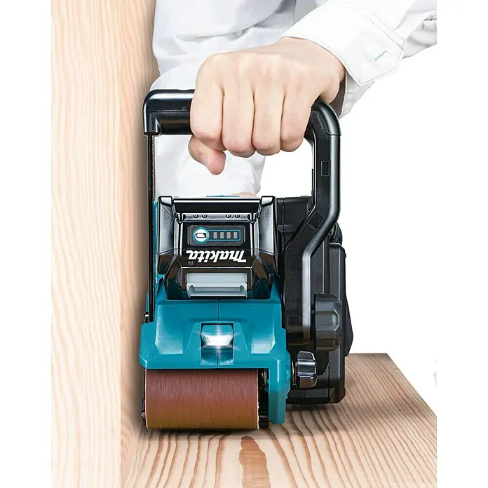 Makita XGT 40V max. Akku-Bandschleifer BS001GZ - 40 V, Ohne Akku - Nahaufnahme eines Makita-Bandschleifers in Aktion, der ein Holzstück bearbeitet. Der Schleifer wird von einer Hand gehalten.