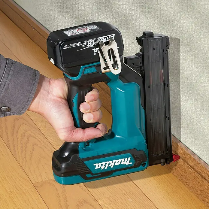 Makita LXT 18V Akku-Nagler Stauchkopfnagler DFN350Z - 18 V, Ohne Akku, Länge Nagel: 15 mm - 35 mm - Bild einer Makita Akku-Nagelpistole mit 18V Akku, die an einer Sockelleiste befestigt wird.\n