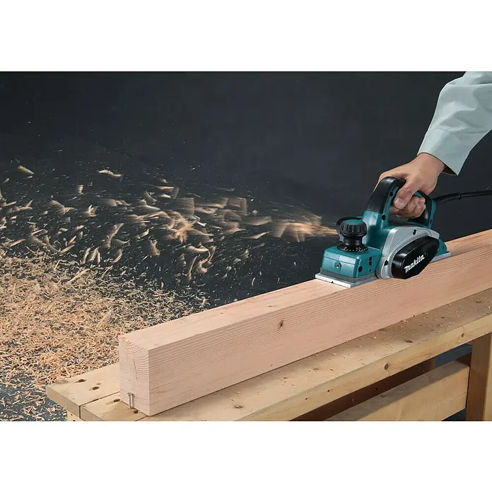 Makita Handhobel im MAKPAC KP0800J - 620 W, Hobelbreite: 82 mm, Falztiefe: 9 mm - Ein Makita Elektrohobel wird verwendet, um Holz zu glätten, wobei Späne in der Luft wirbeln.