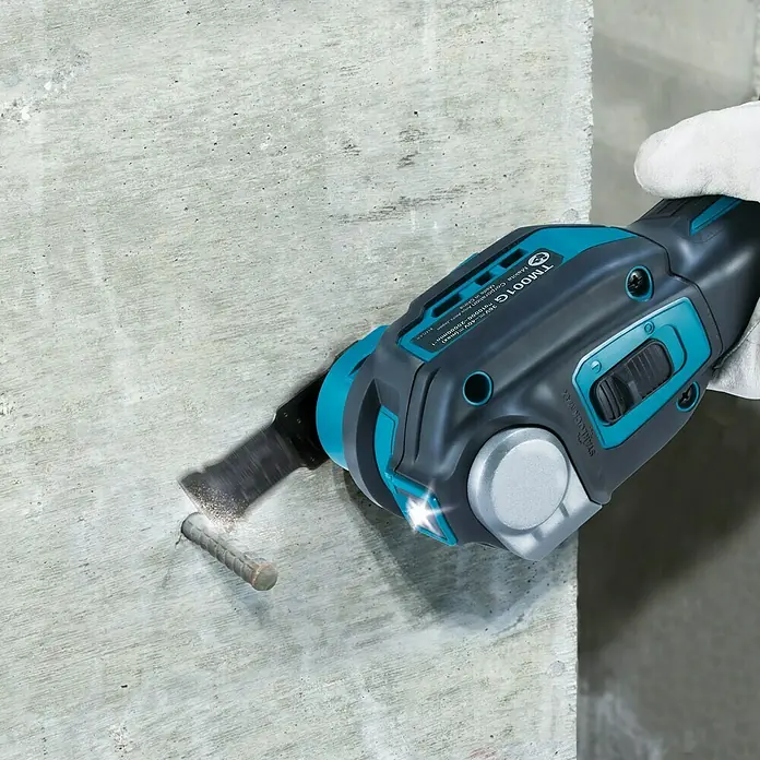 Makita XGT 40V max. Akku-Multifunktionswerkzeug ‎TM001GZ - 40 V, Ohne Akku - Nahaufnahme eines oszillierenden Multifunktionswerkzeugs von Makita beim Schneiden eines Metallstifts in einer Betonwand.