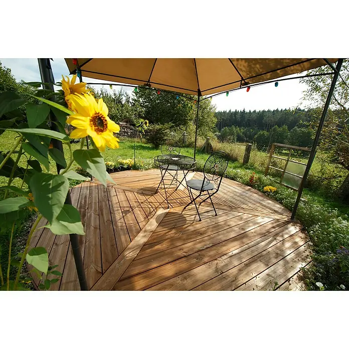 Terrassendiele - Kiefer, 200 x 14,5 x 2,8 cm, Teakfarben - Gemütliche Gartenszene mit einem charmanten Tisch und Stühlen auf einer hölzernen Terrasse, umgeben von blühenden Sonnenblumen.
