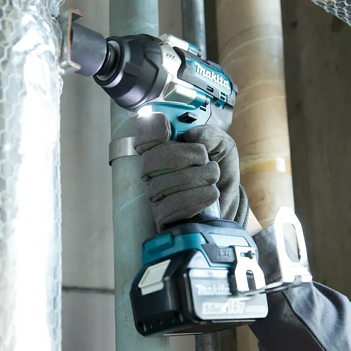 Makita LXT 18V Akku-Schlagschrauber DTW700Z - 18 V, Ohne Akku, 700 Nm, Max. Schlagzahl: 2.700 /min - Nahaufnahme eines Makita Akku-Schlagschraubers mit Arbeitslicht und einer Person mit Arbeitshandschuhen.