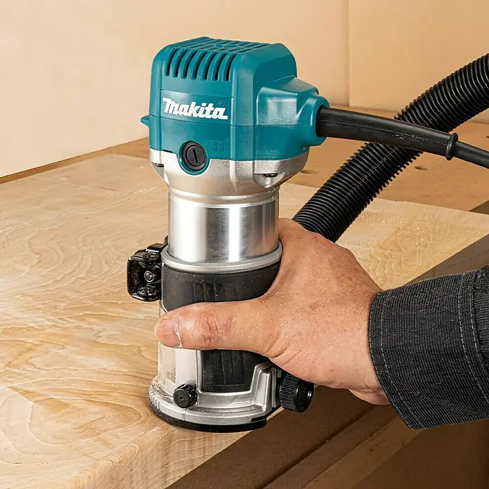 Makita Oberfräse RT0702CX2J - 710 W, 10.000 U/min - 34.000 U/min, Frästiefe: 0 mm - 40 mm - Nahaufnahme einer Makita-Kantenfräse in Aktion, die von einer Hand gehalten wird und Holz bearbeitet.