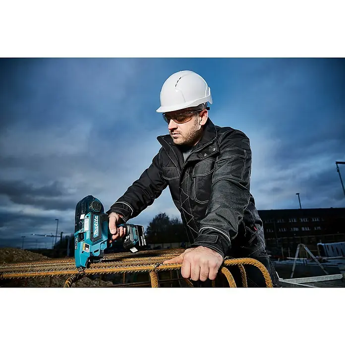 Makita LXT 18V Akku-Bewehrungsverbinder DTR180ZJ - 18 V, Ohne Akku - Ein Bauarbeiter verwendet ein Makita Bindegerät zum Verbinden von Bewehrungsstäben, geschützt durch Helm und Brille auf einer Baustelle.