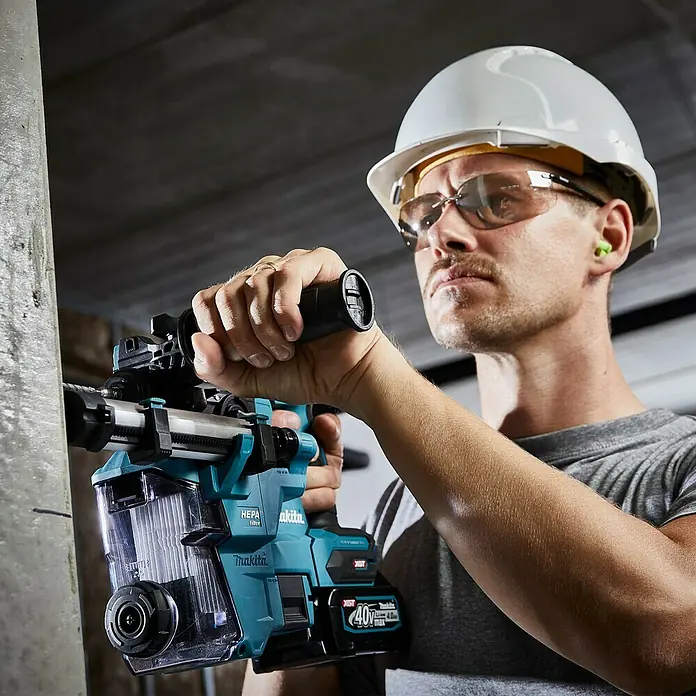 Makita XGT 40V max. Akku-Kombihammer HR010GZ - 40 V, Ohne Akku, 2,1 J - Mann mit Schutzhelm und Brille bedient einen Makita Akku-Bohrhammer mit HEPA-Filter.
