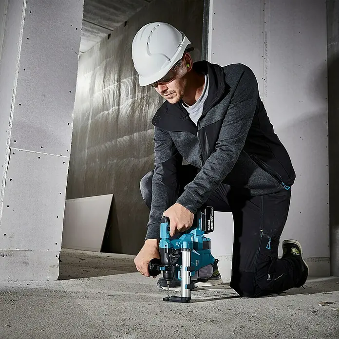 Makita LXT 18V Akku-Bohrhammer DHR183Z - 18 V, Ohne Akku, 1,7 J - Ein Bauarbeiter kniet und bedient eine Makita Kernbohrmaschine für präzise Bohrarbeiten auf einer Baustelle.