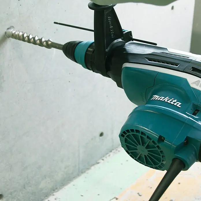 Makita Kombihammer HR5212C - 1.510 W, 20 J, SDS-Max-Aufnahme - Eine Makita Bohrmaschine bohrt ein Loch in eine Betonwand. Sie ist blaugrün und schwarz und hat einen Bohrer mit einer Spirale.