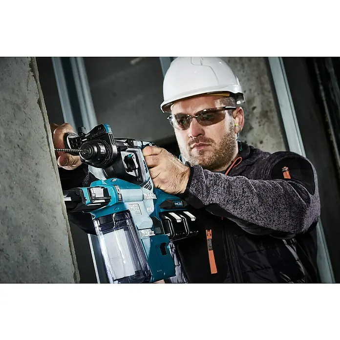 Makita LXT 18V Akku-Kombihammer für SDS-PLUS DHR280ZJ - 36 V, Ohne Akku, Max. Einzelschlagenergie: 2,8 J - Ein Bauarbeiter mit Schutzhelm benutzt einen Makita-Bohrhammer mit Staubabsaugung, um in eine Betonwand zu bohren.
