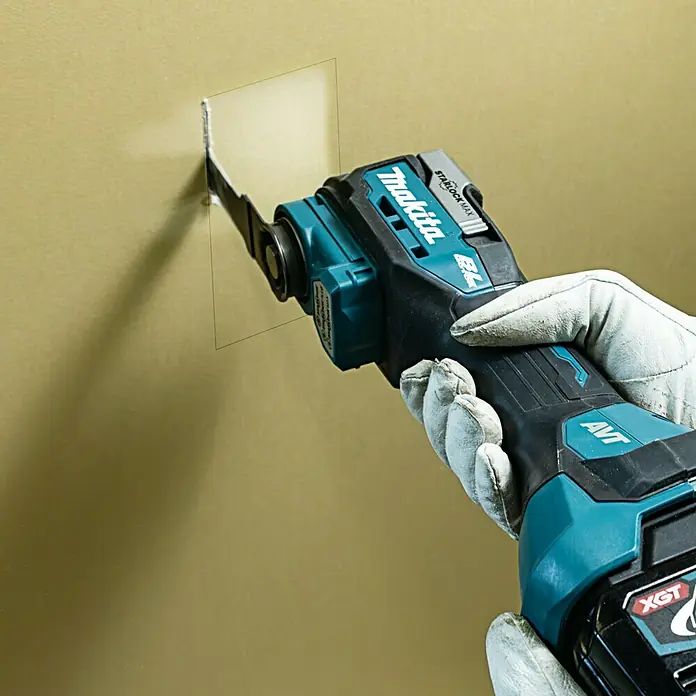 Makita XGT 40V max. Akku-Multifunktionswerkzeug ‎TM001GZ - 40 V, Ohne Akku - Makita Oszillierendes Multifunktionswerkzeug beim Schneiden in eine Wand. Das Werkzeug ist blaugrün und schwarz.