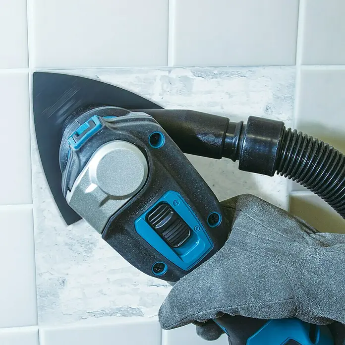 Makita XGT 40V max. Akku-Multifunktionswerkzeug ‎TM001GZ - 40 V, Ohne Akku - Das Bild zeigt einen Multimaster beim Entfernen von Fugen zwischen Fliesen. Der Multimaster ist ein Werkzeug für viele verschiedene Aufgaben.