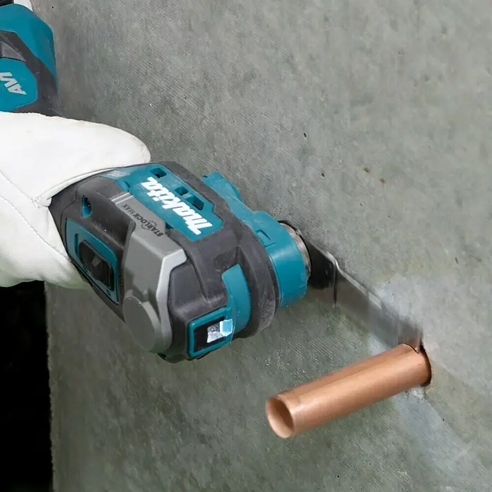 Makita XGT 40V max. Akku-Multifunktionswerkzeug ‎TM001GZ - 40 V, Ohne Akku - Eine Makita oszillierende Multifunktionswerkzeug sägt ein Kupferrohr. Der Benutzer trägt einen weißen Handschuh.