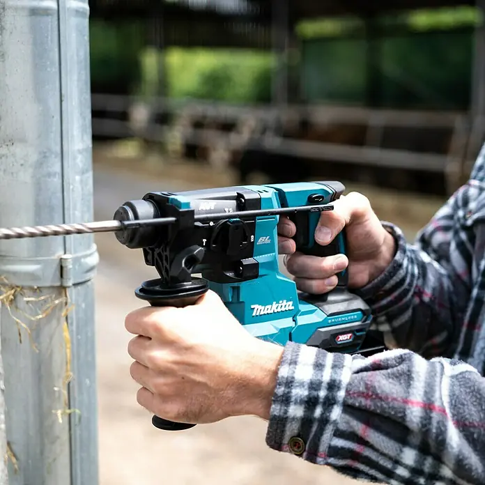 Makita XGT 40V max. Akku-Kombihammer HR010GZ - 40 V, Ohne Akku, 2,1 J - Eine Nahaufnahme eines Makita Akku-Bohrhammers im Einsatz, der ein Loch in einen Metallpfosten bohrt.