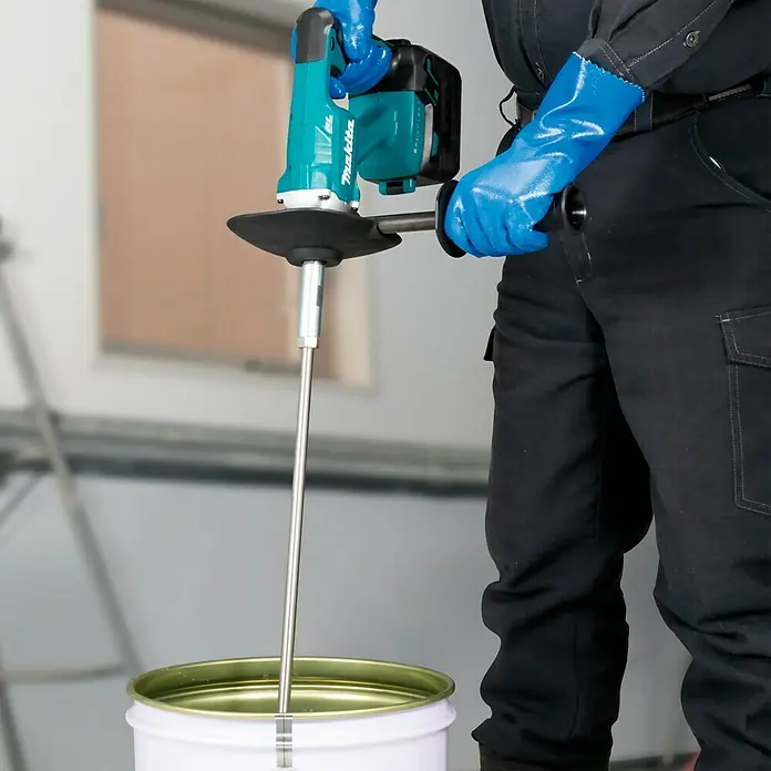 Makita LXT 18V Akku-Rührwerk DUT130Z - 18 V, Ohne Akku - Ein Bauarbeiter mit blauen Handschuhen benutzt einen Makita-Farbenrührer, um Farbe in einem weißen Eimer zu mischen.