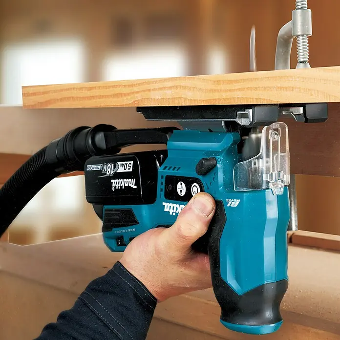 Makita LXT 18V Akku-Pendelhubstichsäge DJV185RF1J - 18 V, Li-Ionen, Anzahl Akkus: 1 Akku, Leerlaufhubzahl: 800 /min - 3.000 /min - Aufnahme einer Akku-Nutfräse von Makita in Aktion. Das Werkzeug ist auf ein Holzstück montiert und wird von einer Hand gehalten.