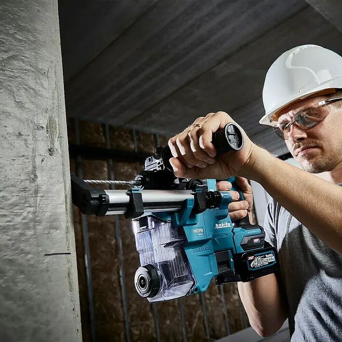 Makita XGT 40V max. Akku-Kombihammer HR010GZ - 40 V, Ohne Akku, 2,1 J - Ein Bauarbeiter mit Schutzhelm und Brille benutzt einen Makita Bohrhammer mit Staubabsaugung an einer Betonwand.