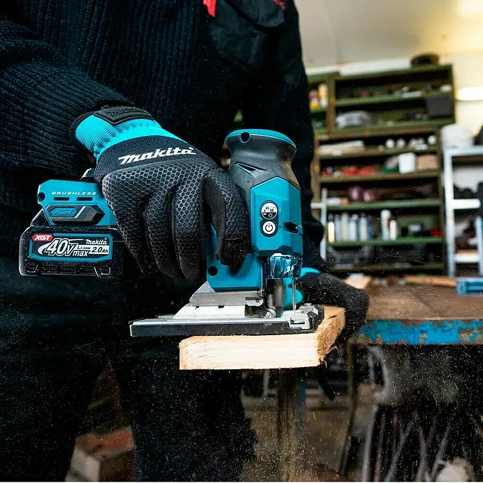 Makita XGT 40V max. Akku-Pendelhubstichsäge JV001GZ - 40 V, Ohne Akku, Leerlaufhubzahl: 800 /min - 3.500 /min - Nahaufnahme einer Makita Akku-Stichsäge beim Sägen eines Holzstücks, bedient von einer Person mit Makita-Handschuhen.
