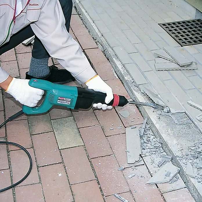 Makita Meißelhammer HK0500 - 550 W, Max. Schlagzahl: 3.500 U/min, 1,8 J - Abgebildet ist ein Arbeiter, der mit einem Makita Abbruchhammer Beton aufbricht, wobei der Fokus auf dem Werkzeug und seiner Anwendung liegt.