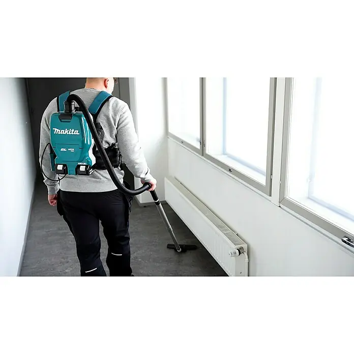 Makita LXT 18V Akku-Rucksackstaubsauger DVC261ZX15 - 36 V, Ohne Akku, Behältervolumen: 2 l - Eine Person trägt einen Makita-Rucksackstaubsauger, während sie einen Flur saugt. Der Staubsauger ist blaugrün und schwarz.