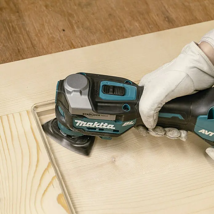 Makita XGT 40V max. Akku-Multifunktionswerkzeug ‎TM001GZ - 40 V, Ohne Akku - Nahaufnahme eines Makita Multifunktionswerkzeugs beim Schleifen eines Holzstücks mit Handschuhen für präzise Holzarbeiten.