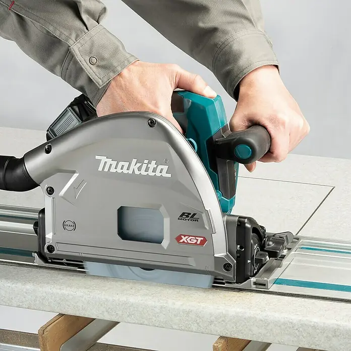 Makita XGT 40V max. Akku-Tauchsäge im MAKPAC SP001GZ03 - 40 V, Ohne Akku, Durchmesser Sägeblatt: 165 mm, 2.500 U/min - Ein Mann bedient eine Makita Tauchsäge auf einer Werkbank. Die Tauchsäge ist silbern und blaugrün.