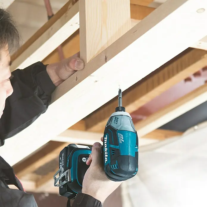 Makita LXT 18V Akku-Impulsschrauber DTS141Z - 18 V, Ohne Akku, 40 Nm - Ein Makita Akku-Schlagschrauber wird verwendet, um ein Holzstück zu befestigen. Das Elektrowerkzeug ist blaugrün und schwarz.