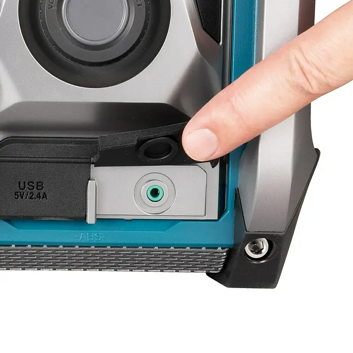 Makita Akku-Baustellenradio MR007GZ - 40 V, Ohne Akku, 87,5 - 108 MHz (UKW/FM) - Nahaufnahme eines Makita-Radios mit USB-Anschluss, Aux-Eingang und einer Hand, die auf die Schutzabdeckung drückt.