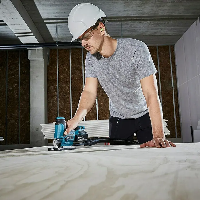 Makita LXT 18V Akku-Pendelhubstichsäge DJV185RF1J - 18 V, Li-Ionen, Anzahl Akkus: 1 Akku, Leerlaufhubzahl: 800 /min - 3.000 /min - Ein Handwerker mit Schutzbrille und Helm bedient eine Makita Akku-Stichsäge auf einer Holzplatte.