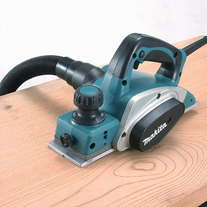 Makita Handhobel im MAKPAC KP0800J - 620 W, Hobelbreite: 82 mm, Falztiefe: 9 mm - Ein Makita Elektrohobel in Türkis und Silber steht auf einem Holzbrett. Der Hobel hat einen Staubsaugeranschluss.