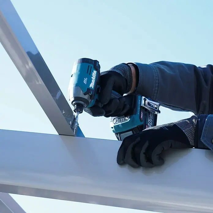 Makita XGT 40V max. Akku-Schlagschrauber TD003GZ - 40 V, Ohne Akku, 210 Nm - Nahaufnahme eines Akku-Schlagschraubers von Makita in Aktion, der an einer Metallkonstruktion arbeitet, bedient von einer Person mit Arbeitshandschuhen.
