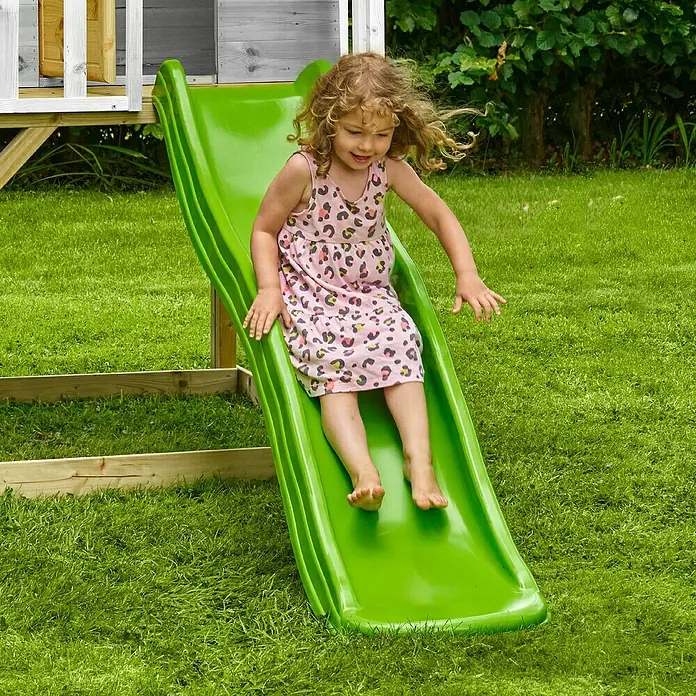 Zwerkules Spielhaus Valli - L x B x H: 270 x 148 x 244 cm, Holz, Natur/Grau, Mit Stelzen & Rutsche - Ein fröhliches Mädchen saust auf einer leuchtend grünen Kinderrutsche herunter, eingebettet in einen sonnigen Garten.